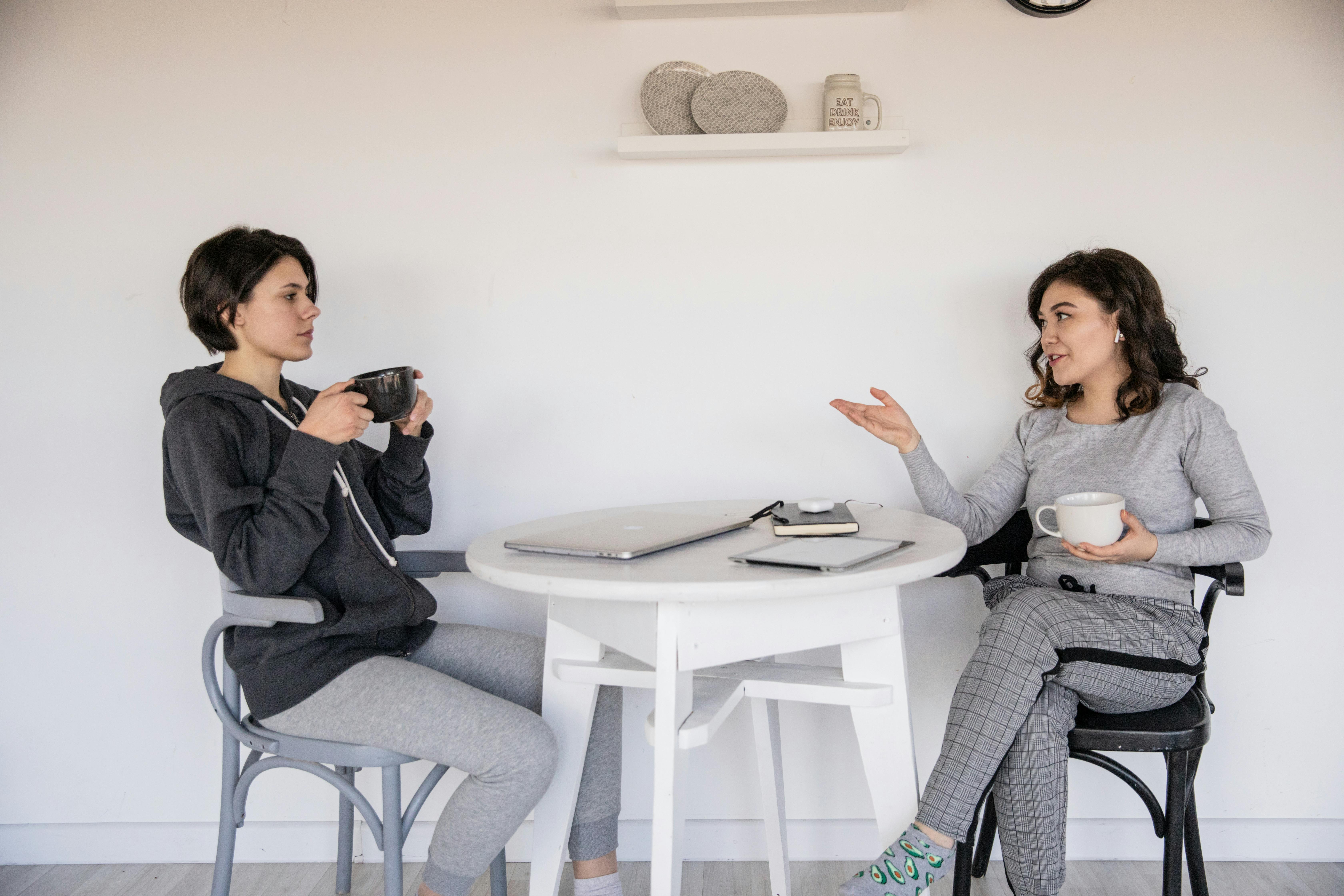 Two women enjoying a casual conversation over coffee in a cozy indoor setting, strengthening their connection.